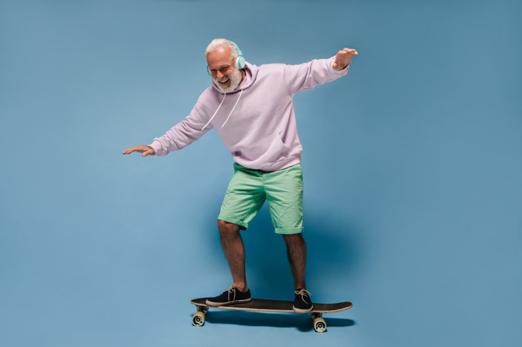 Shot of man in green shorts and hoodie riding skate board. Positive guy with beard and headphones p